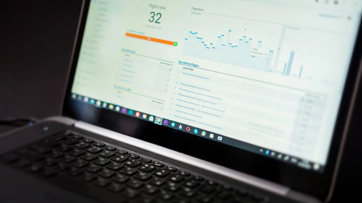 A laptop on a dark desk showing a real-time web analytics dashboard with active user counts, a pageviews graph, and a list of top active pages
