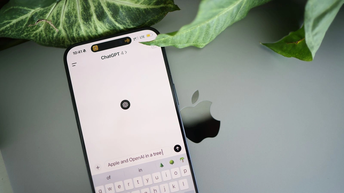 A smartphone resting on a laptop lid with the ChatGPT app open and a question half typed